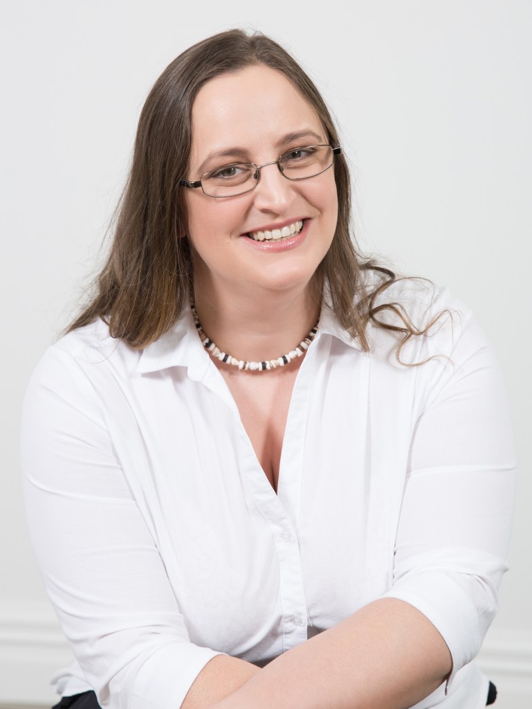 Smiling woman with brown hair and glasses in a white shirt.
