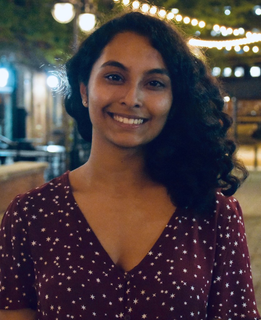 Smiling woman with shoulder-length curly black hair and a v-neck maroon blouse with white stars.